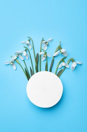 Beautiful snowdrops and paper card on light blue background, flat lay. Space for text