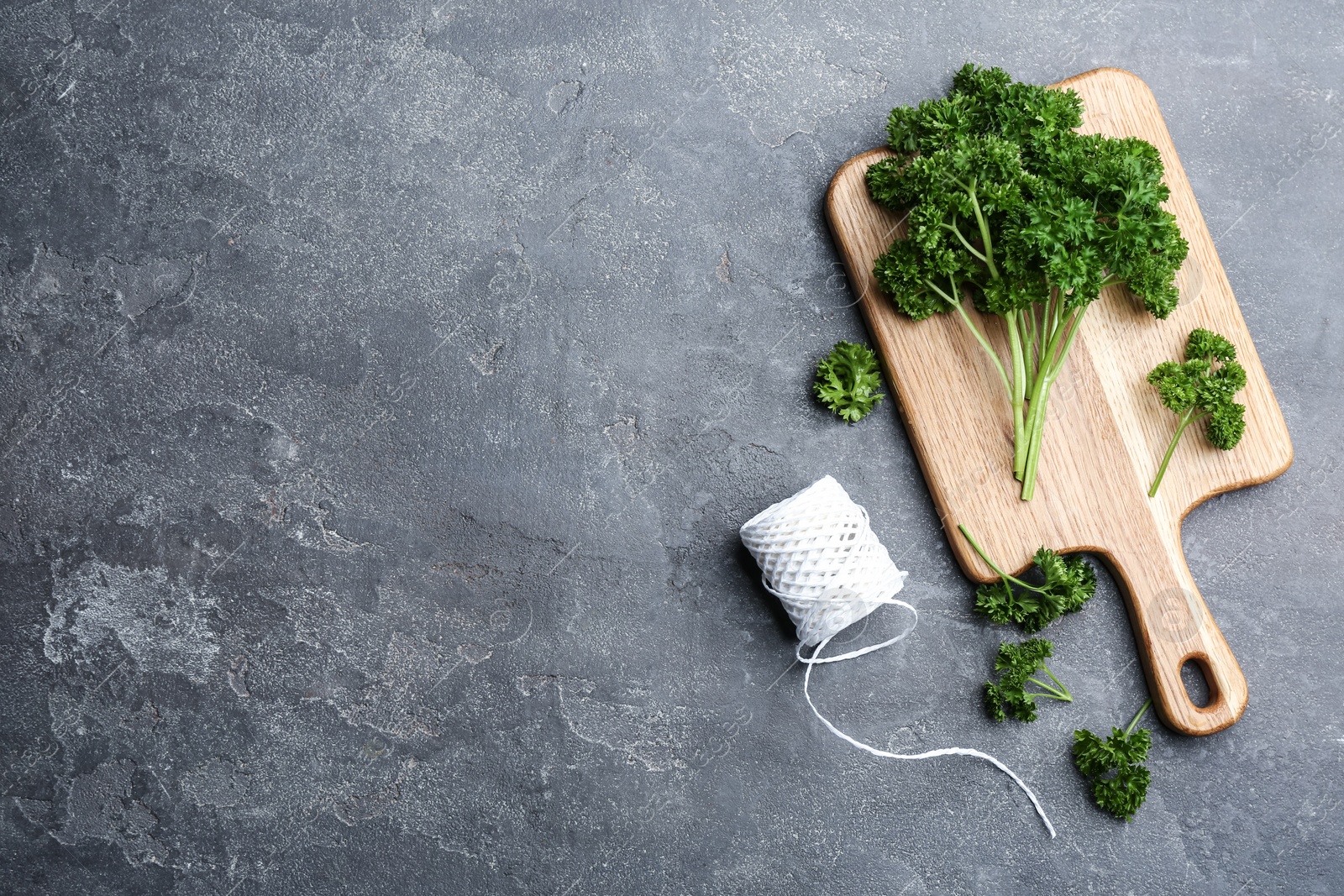 Photo of Fresh curly parsley, cutting board and rope on grey table, flat lay. Space for text