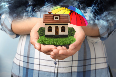 Image of Insurance concept - umbrella demonstrating protection. Woman holding house model with green lawn, closeup