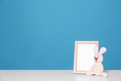 Photo of Photo frame and adorable toy bunny on table against color background, space for text. Child room elements