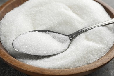 Photo of Granulated sugar in bowl and spoon on table, closeup