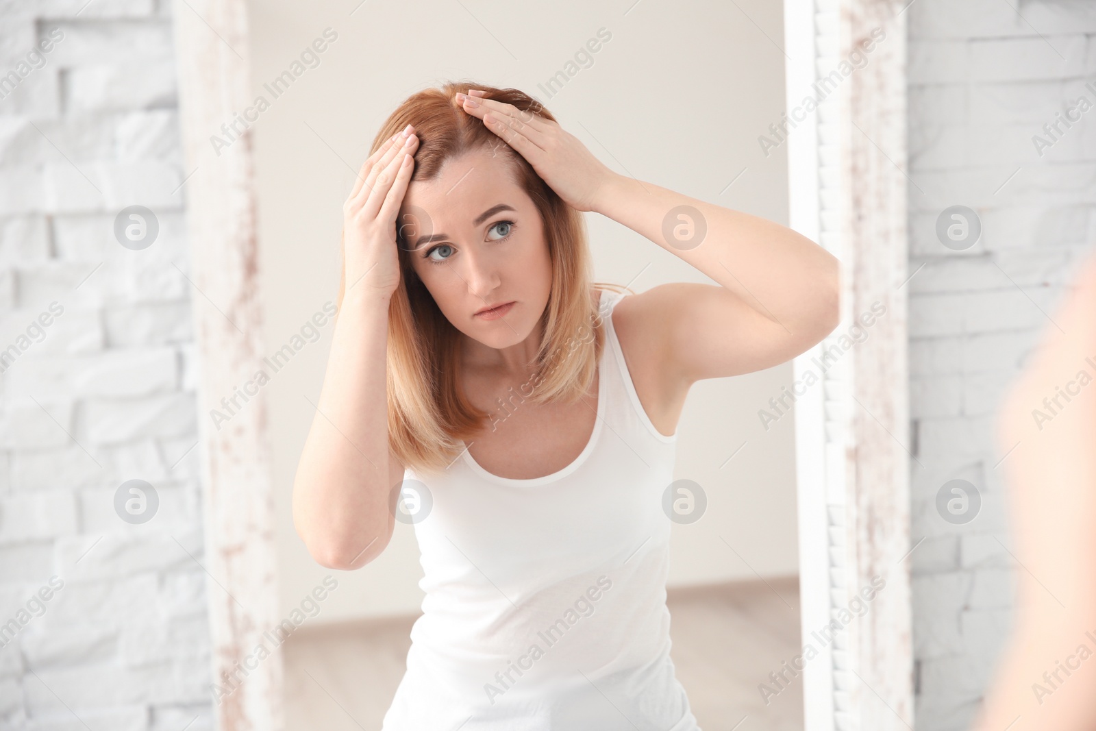 Photo of Young woman with hair loss problem in front of mirror at home