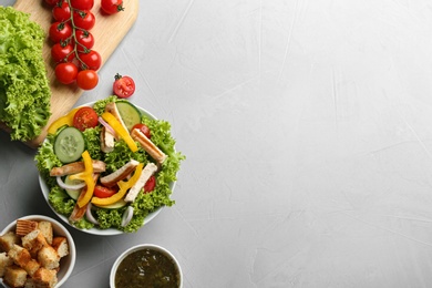 Photo of Delicious chicken salad and fresh vegetables on grey table, flat lay. Space for text