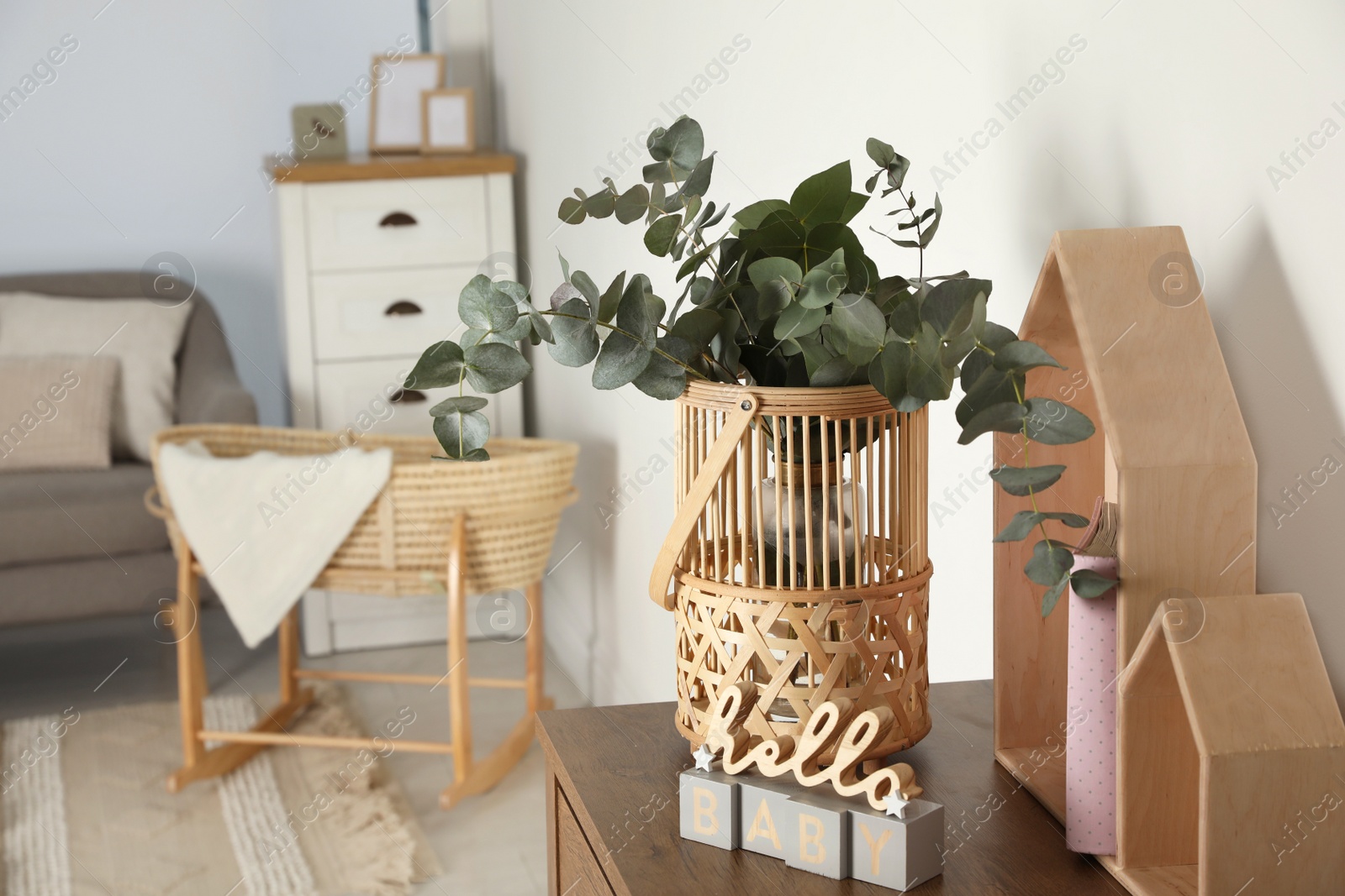 Photo of Wicker basket with beautiful eucalyptus branches and phrase Hello Baby on wooden table indoors, space for text. Interior design