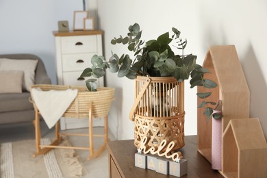 Photo of Wicker basket with beautiful eucalyptus branches and phrase Hello Baby on wooden table indoors, space for text. Interior design