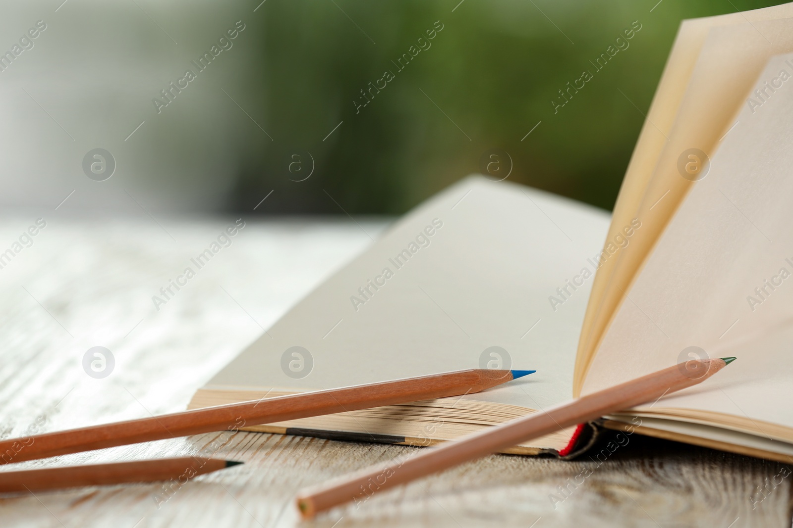 Photo of Closeup view of open notebook with pencils on white wooden table against blurred background