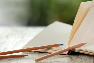 Photo of Closeup view of open notebook with pencils on white wooden table against blurred background