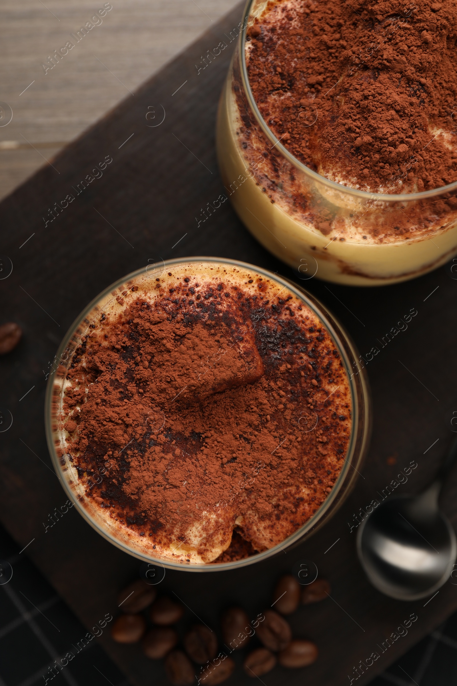 Photo of Delicious tiramisu in glasses and coffee beans on table, top view