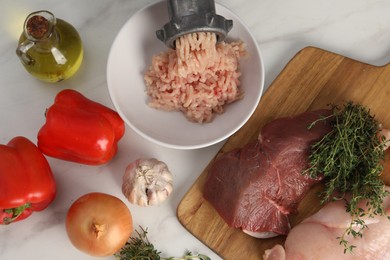Photo of Metal meat grinder with chicken mince and products on white marble table, flat lay
