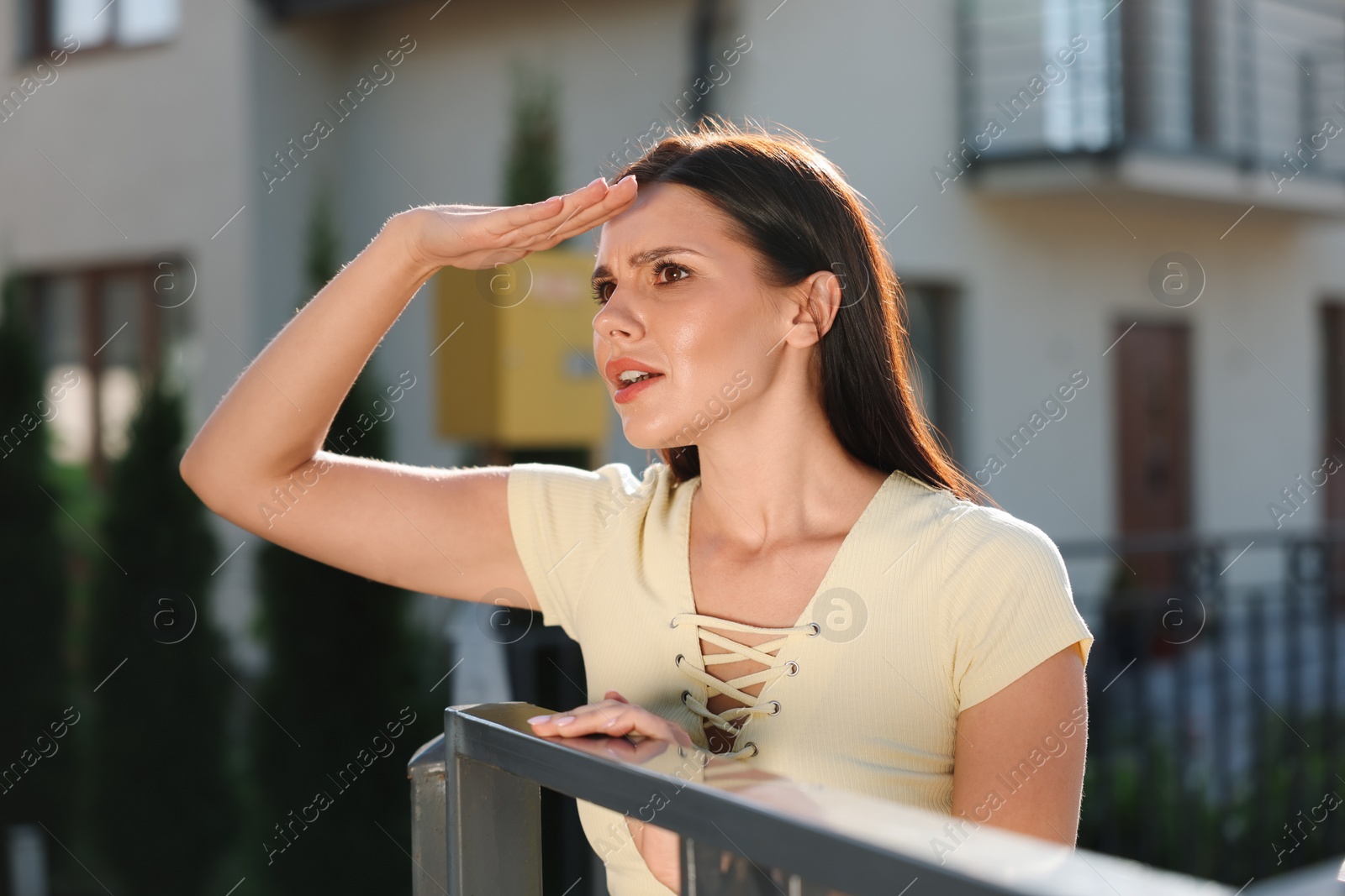 Photo of Concept of private life. Curious young woman spying on neighbours over fence outdoors