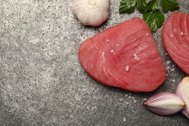 Raw tuna fillets with salt, parsley and shallot on gray table, flat lay. Space for text