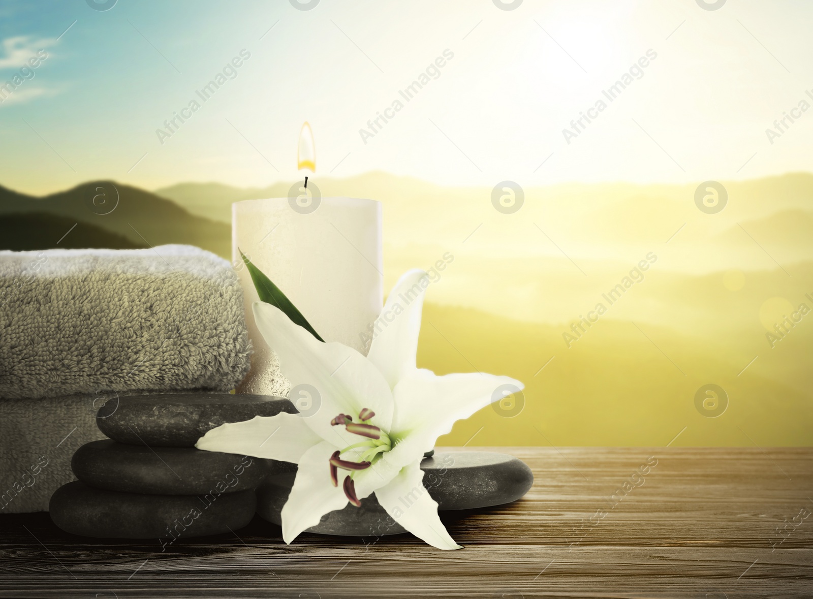 Image of Composition with spa stones, towels and flower on wooden table against beautiful mountain landscape in morning, space for text