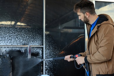 Photo of Man cleaning auto mats with high pressure water jet at self-service car wash