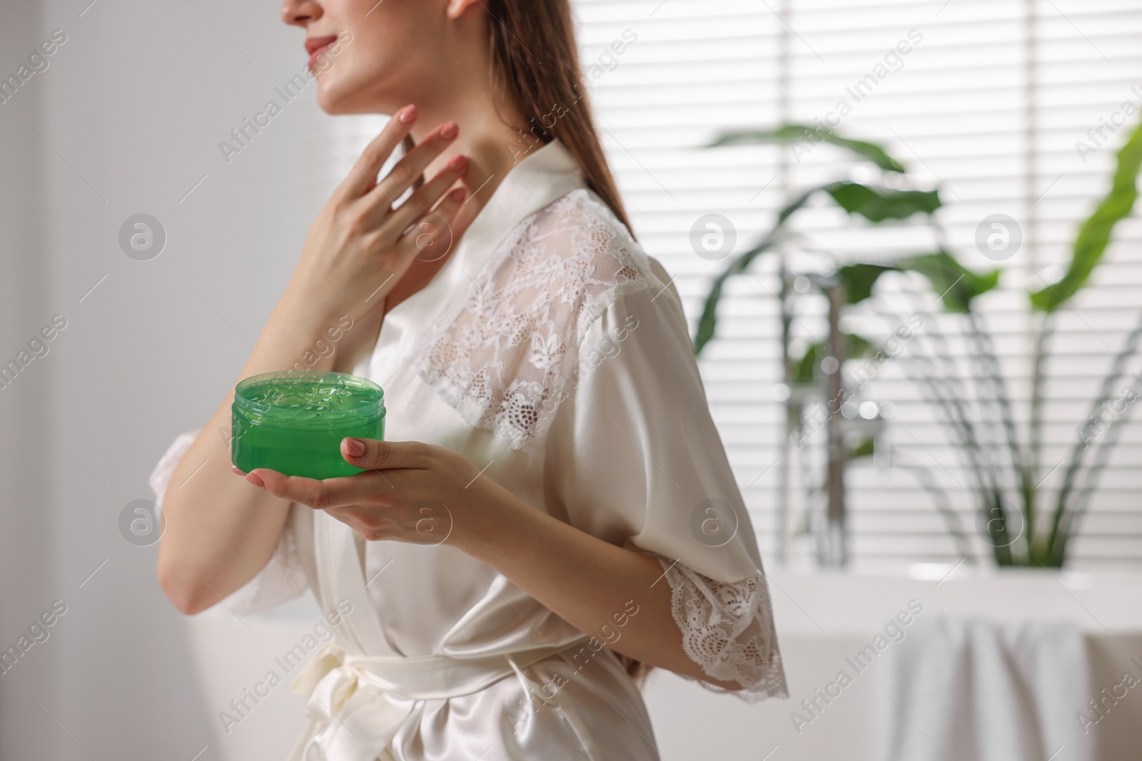 Photo of Young woman applying aloe gel onto her neck in bathroom, closeup. Space for text