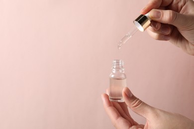 Photo of Woman dripping cosmetic serum from pipette into bottle on light pink background, closeup. Space for text