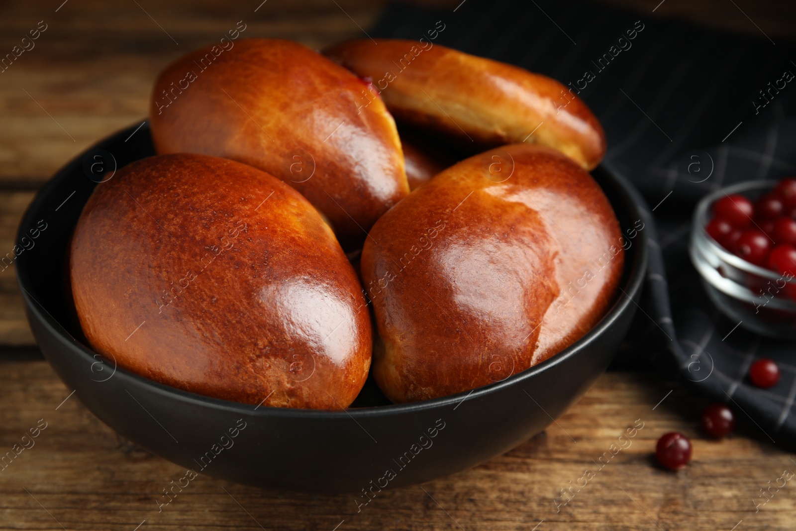 Photo of Delicious baked cranberry pirozhki in bowl on wooden table