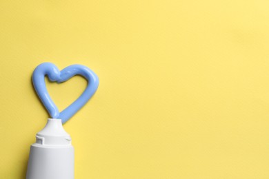 Photo of Blank tube and heart made with toothpaste on yellow background, flat lay. Space for text