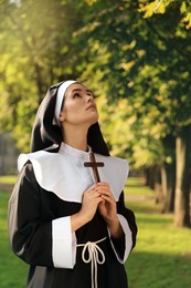 Young nun with Christian cross in park on sunny day