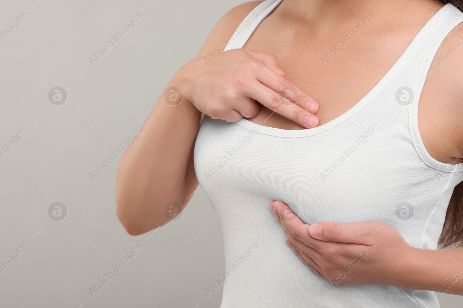 Photo of Woman doing breast self-examination on light grey background, closeup