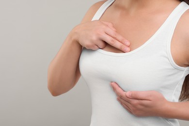 Photo of Woman doing breast self-examination on light grey background, closeup