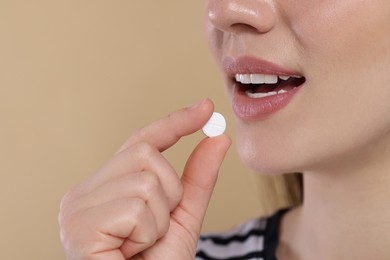 Photo of Woman taking pill on beige background, closeup