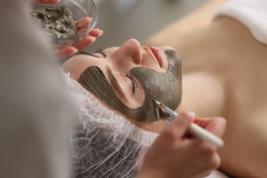 Cosmetologist applying mask on woman's face, closeup