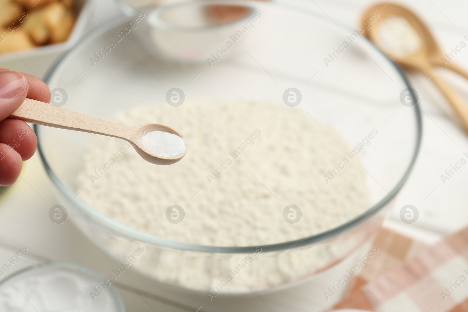 Photo of Woman taking spoon with baking powder from bowl at white table, closeup