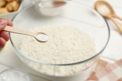 Woman taking spoon with baking powder from bowl at white table, closeup