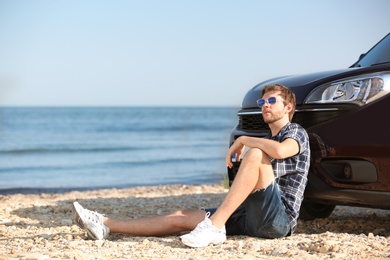 Young man near car on beach. Space for text