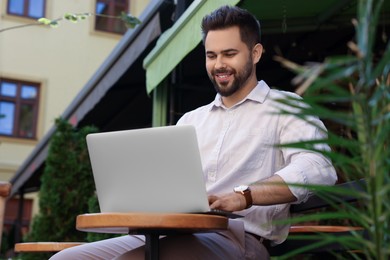 Photo of Handsome young man working on laptop at table in outdoor cafe