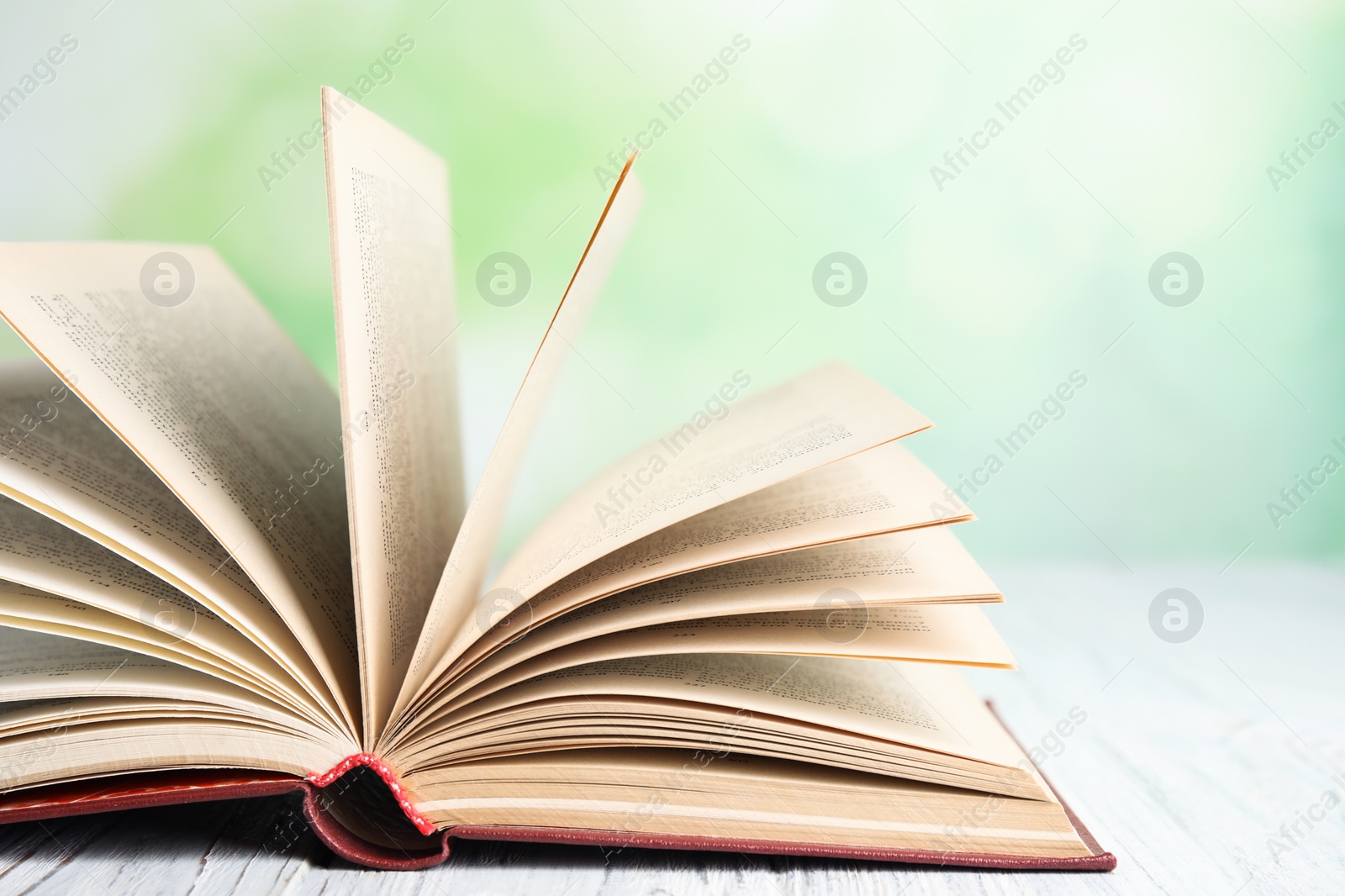 Photo of Open book on white wooden table against blurred green background, closeup