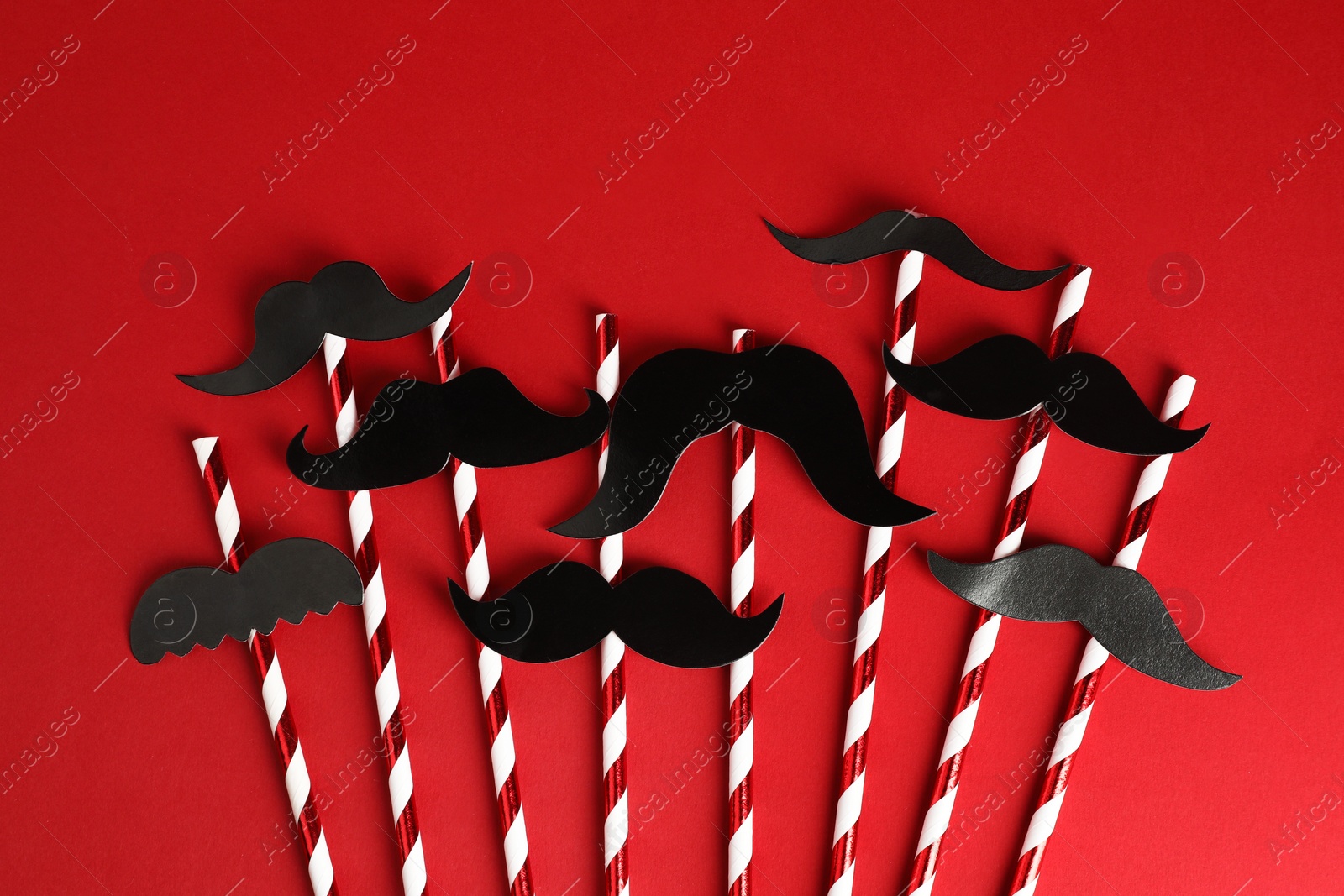 Photo of Fake paper mustaches with party props on red background, flat lay