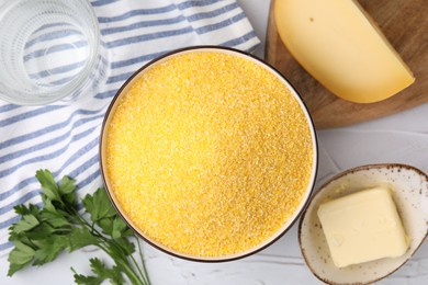 Photo of Raw cornmeal in bowl, water, cheese, parsley and butter on light table, flat lay