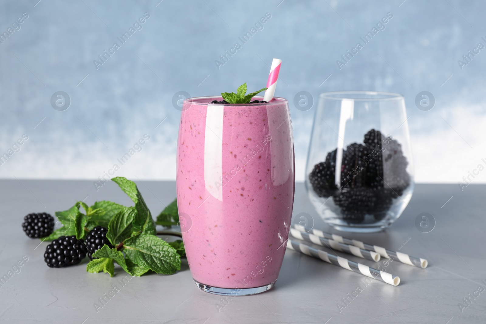Photo of Glass of tasty blackberry smoothie and ingredients on grey table