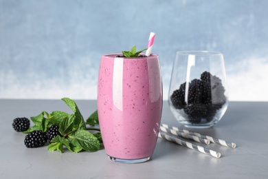 Glass of tasty blackberry smoothie and ingredients on grey table