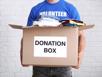 Photo of Male volunteer holding donation box with clothes indoors