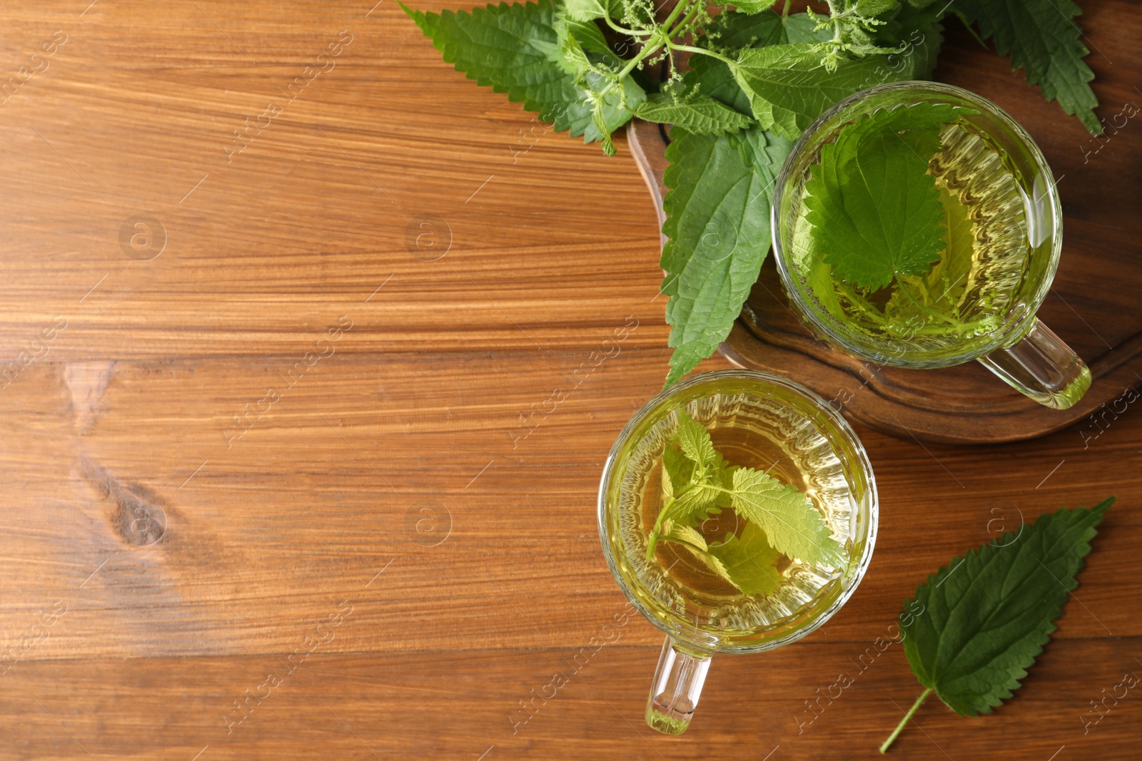 Photo of Aromatic nettle tea and green leaves on wooden table, flat lay. Space for text