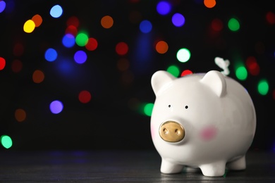 Photo of Piggy bank on wooden table against blurred Christmas lights, space for text