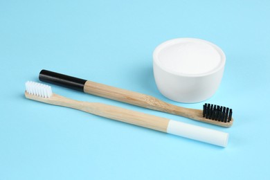 Photo of Bamboo toothbrushes and bowl with baking soda on light blue background