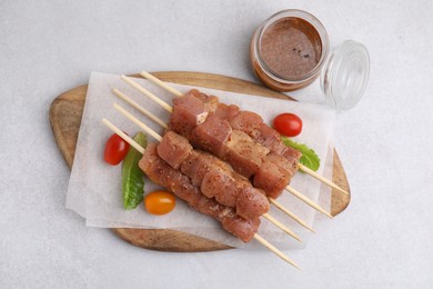 Photo of Wooden skewers with cut raw marinated meat on light grey table, flat lay