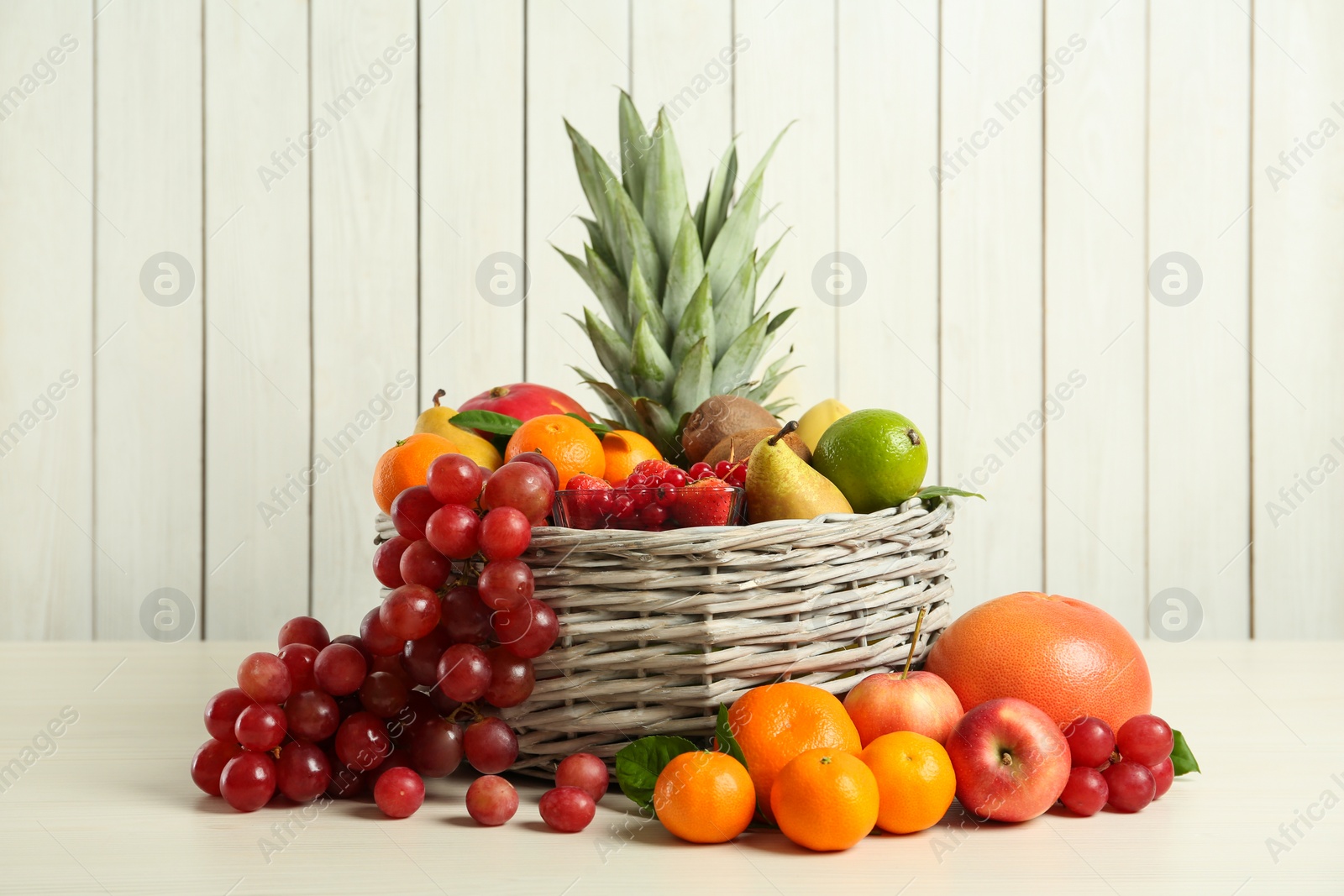 Photo of Wicker basket with different fresh fruits on white wooden table