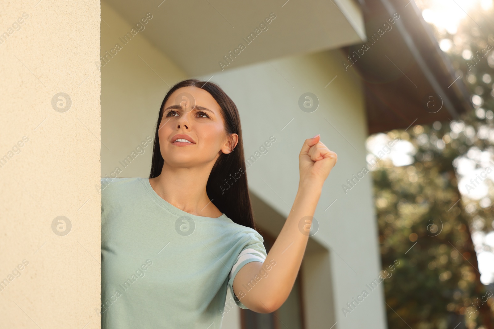 Photo of Angry young woman showing fist near house. Annoying neighbour