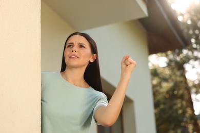 Photo of Angry young woman showing fist near house. Annoying neighbour