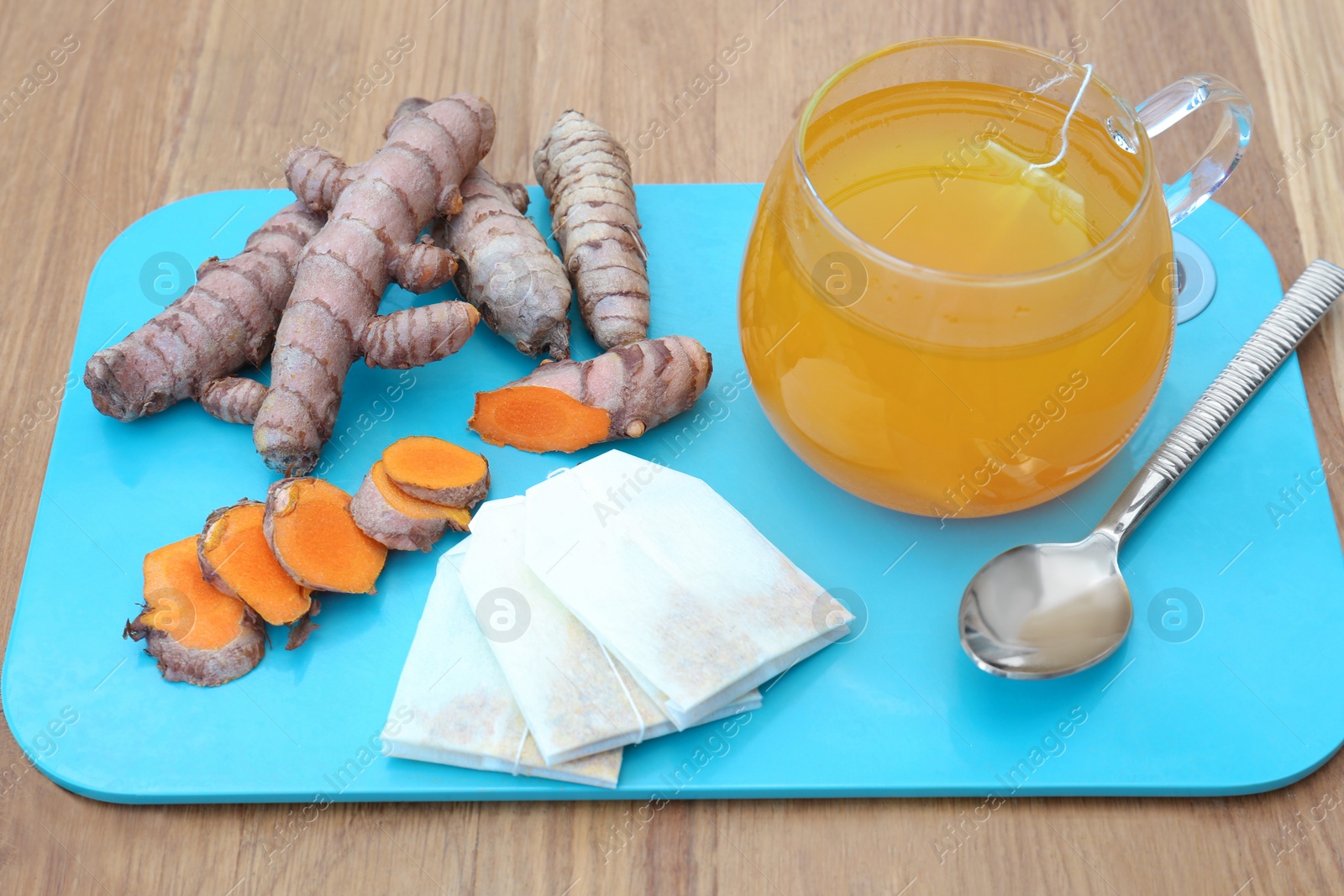 Photo of Tray with glass cup of hot tea and turmeric roots on wooden table