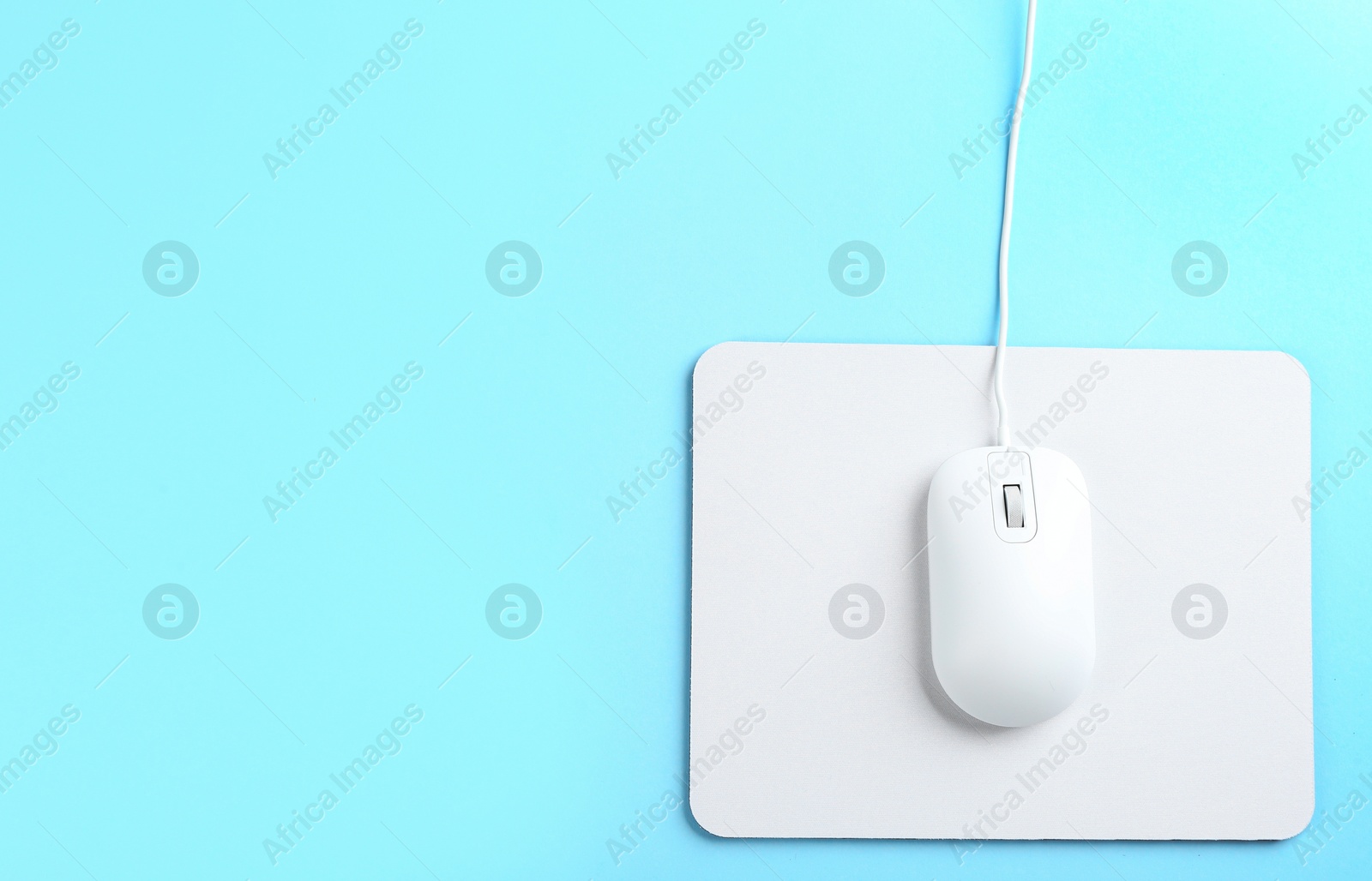 Photo of Modern wired mouse and white pad on light blue background, top view. Space for text
