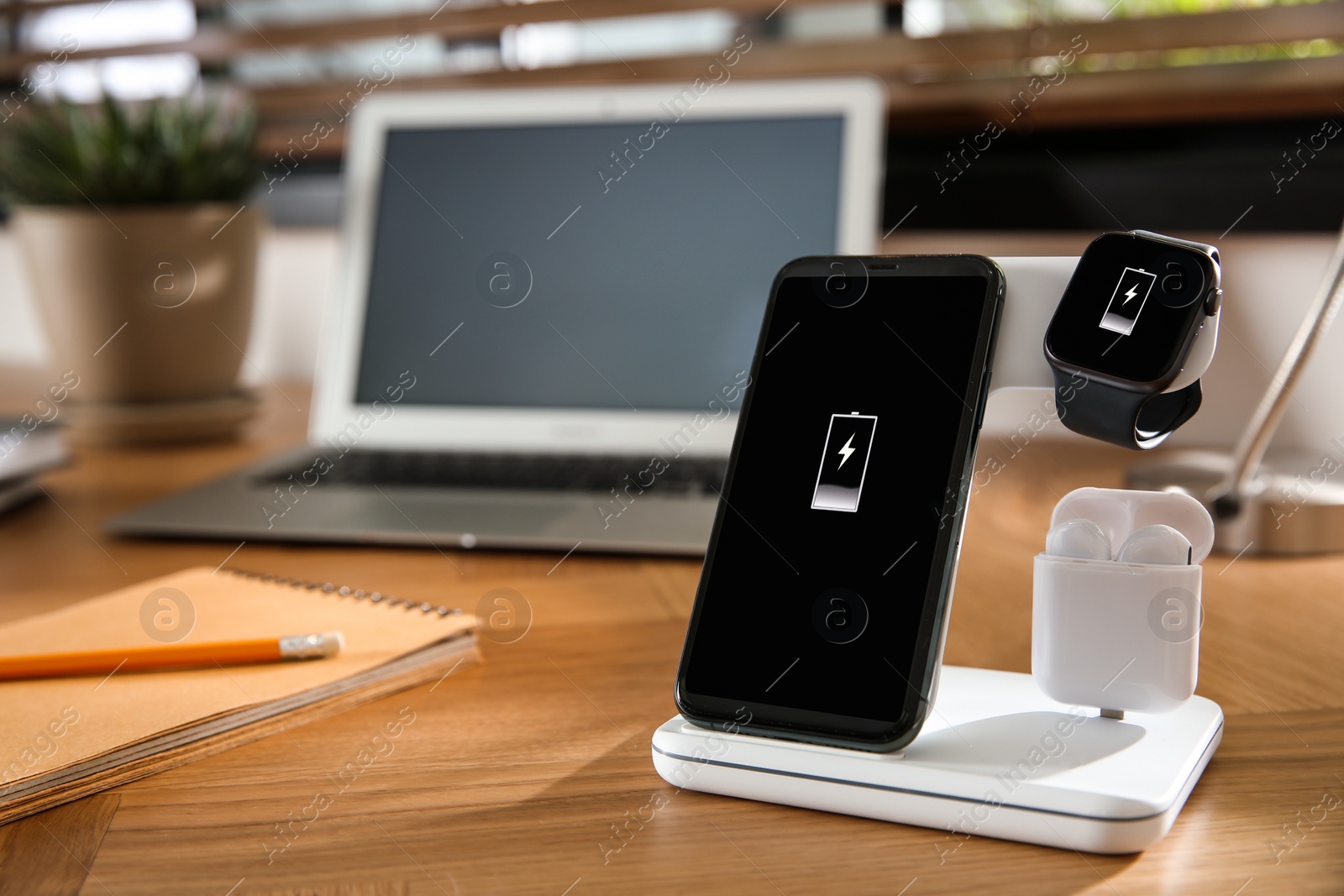 Photo of Mobile phone, earphones and smartwatch charging with wireless pad on wooden desk, space for text. Modern workplace device