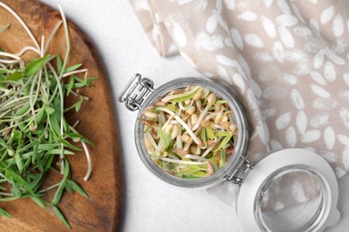 Photo of Mung bean sprouts in glass jar and wooden board on light table, flat lay