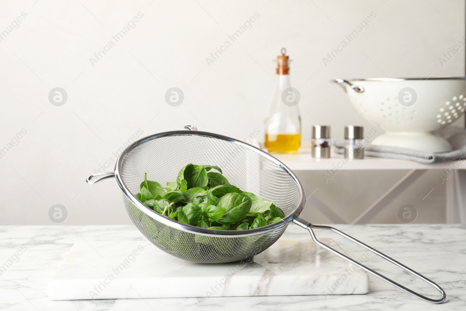 Photo of Sieve with fresh green basil leaves on table in kitchen