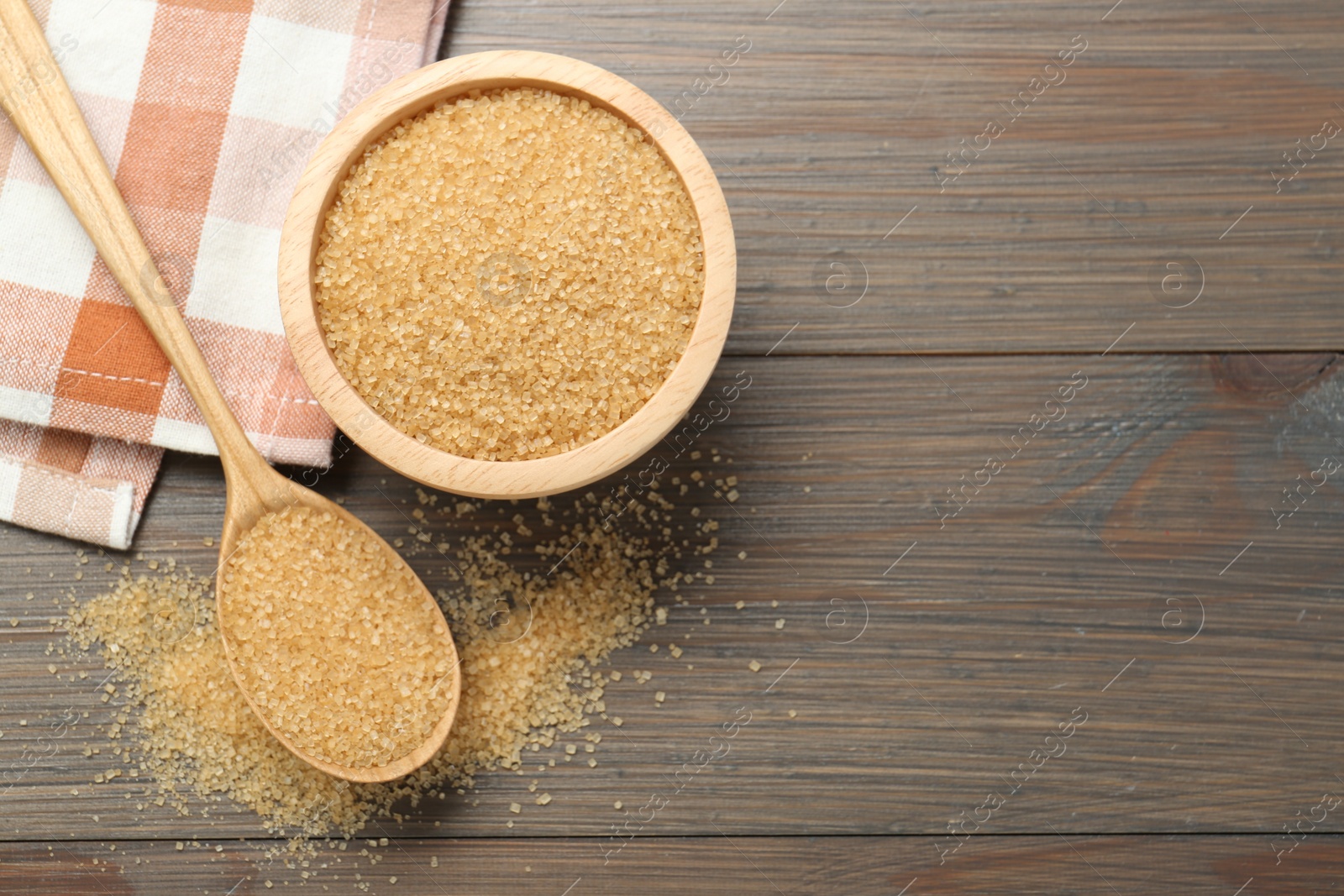 Photo of Brown sugar in bowl and spoon on wooden table, flat lay. Space for text