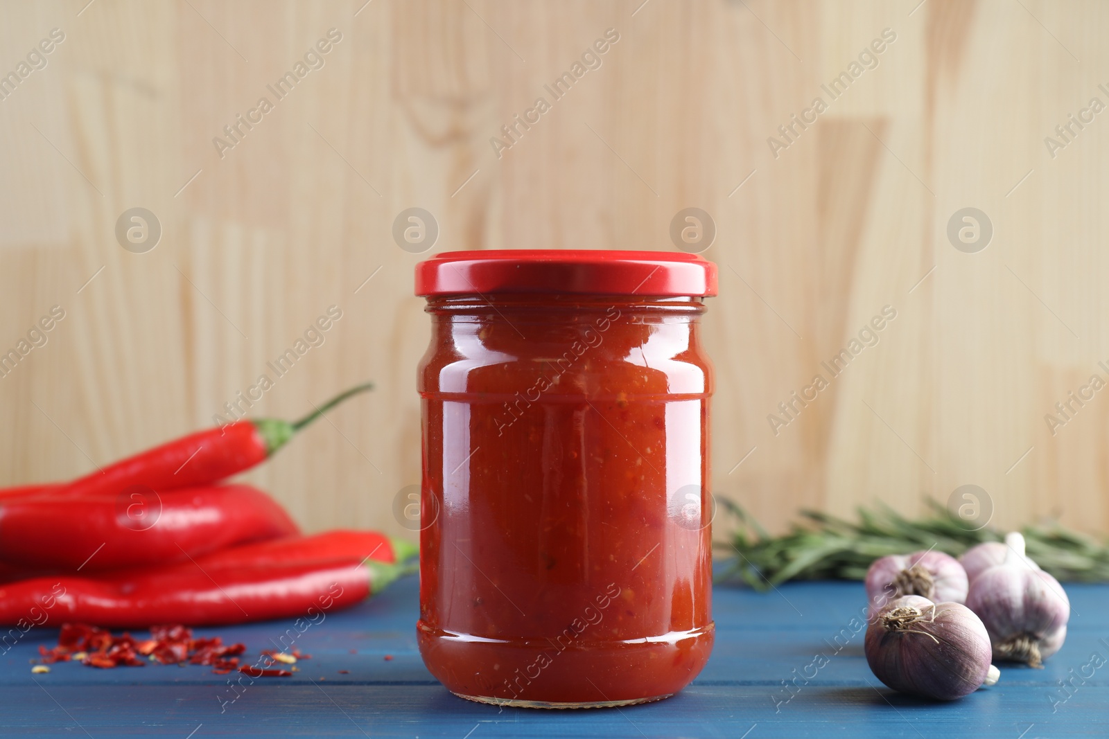 Photo of Spicy chili sauce in jar, garlic and peppers on blue wooden table